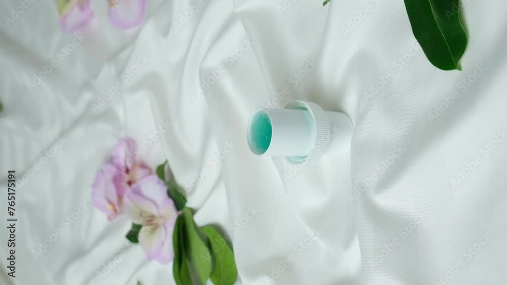 Laundry detergent or fabric softener poured into lid, falling flowers, vertical slow motion Laundry detergent or fabric softener poured into lid, falling flowers, vertical slow motion