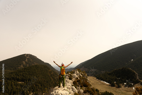 A person is standing on a mountain top, looking out over the landscape. The sky is cloudy and the mountains are in the background. The person appears to be happy and content, enjoying the view