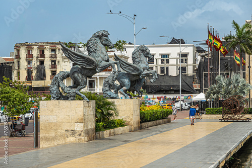 Cartagena, Colombia - July 25, 2023: Double Pegasus statues at end of old town dock with generic architecture buildings in back. National flags behind photo