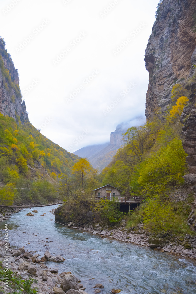 A small house near a mountain river and the foot of the misty mountains. North Caucasus, Russia.