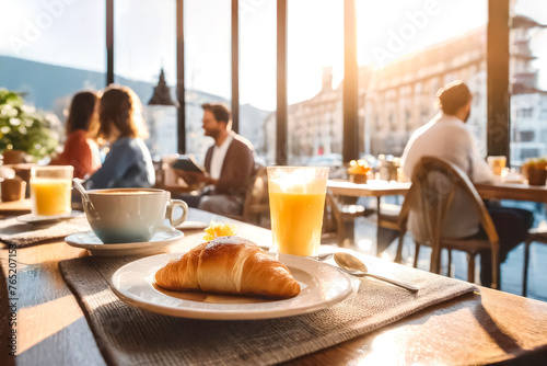 Im Vordergrund ein Croissant, im Hintergrund ein Cafe mit Gästen 