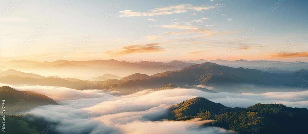 A breathtaking aerial view of a mountain range engulfed in clouds at sunset, with the suns warm light creating a stunning afterglow in the atmosphere