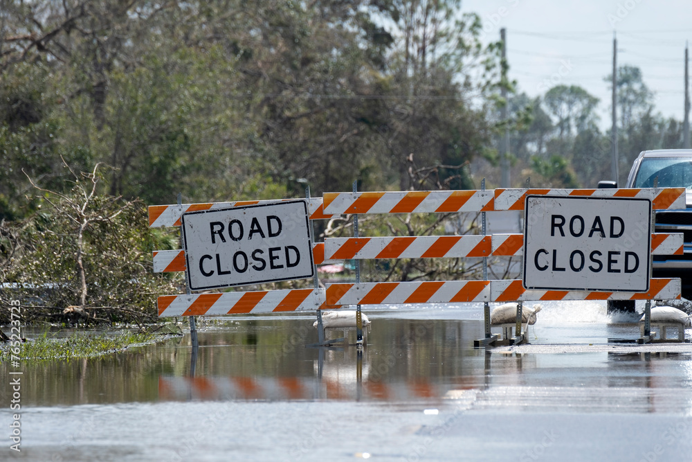 Flooded street in Florida after hurricane rainfall with road closed signs blocking driving of cars. Safety of transportation during natural disaster concept