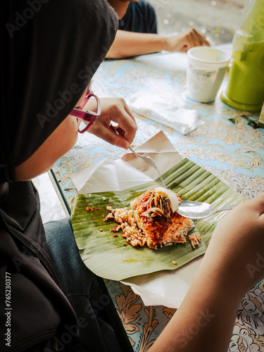 Eating asian food nasi lemak on banana leaf as breakfast, rear view.