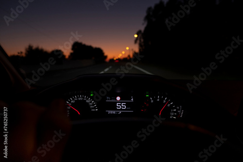 Driver view to the speedometer at 55 kmh or 55 mph, on a road blurred in motion, night fall view from inside a car of driver POV of the road landscape.