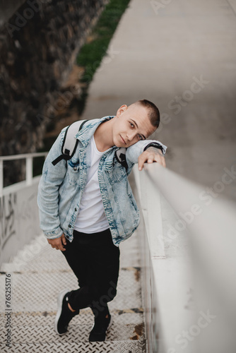 Canvas Print A young man in a blue jacket and black pants is leaning against a white railing