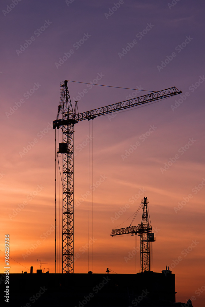 Shadows of two construction cranes on a sunset background. Shadows of two construction cranes on a sunset background.