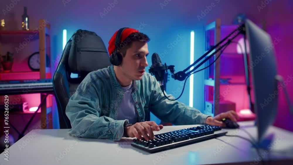 Young hipster man wearing headphones playing computer game neon fashion room, loser. male gamer lose hard match, looking at computer monitor, using computer mouse and keyboard. Cybersport, gaming club Young hipster man wearing headphones playing computer game neon fashion room, loser. male gamer lose hard match, looking at computer monitor, using computer mouse and keyboard. Cybersport, gaming club