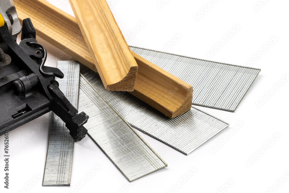 The hammer of a power nail gun with a variety of strips of finishing nails or brads in various lengths and pieces of wood trim molding isolated on white - obrazy, fototapety, plakaty 