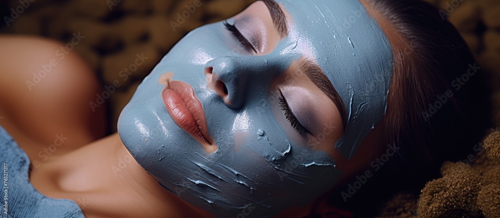Fototapeta premium The woman is reclined with an electric blue mask covering her face. She resembles a fictional character in an art animation event. Her thumb is resting on her jaw. It looks fun