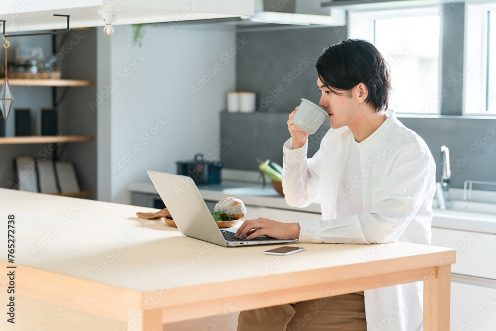 家で朝食を食べながらパソコンを使う若いアジア人男性
