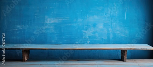 An aged wooden bench is placed against a blue-painted wall in an indoor setting