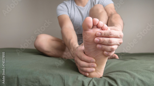 Person massaging their foot due to pain in the sole, arch and toes. Space for text on the left. photo