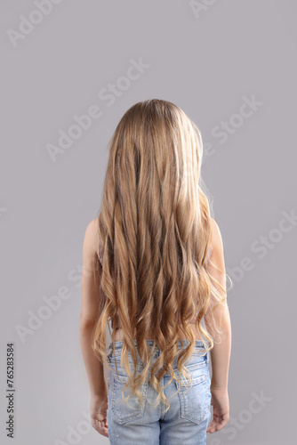 Little girl with wavy hair on grey background, back view