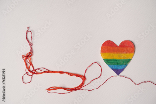 corazón pintado con arcoíris y unido a un hilo rojo