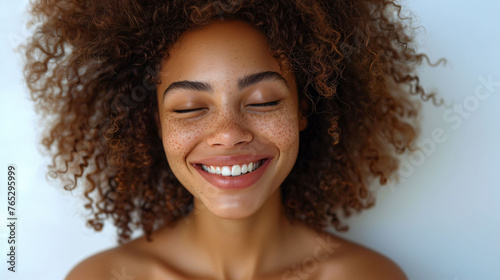 Portrait of a joyful young woman with a white smile curly hair and freckles on her face, looking contented and happy.
