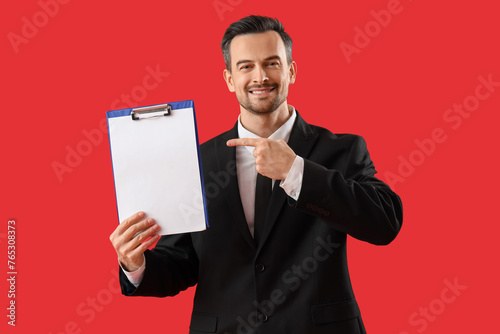 Portrait of male businessman pointing at blank clipboard on red background