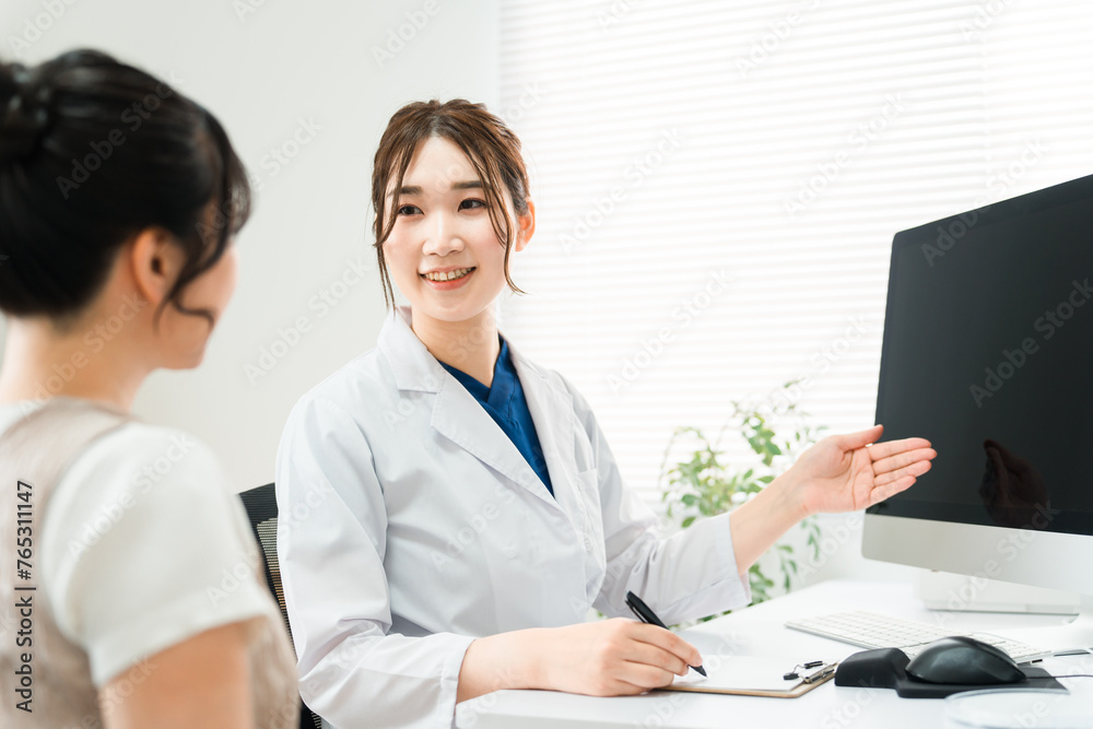 病院・クリニックでパソコンを使って診察・診療・説明・問診をする医師・医者の女性と患者

