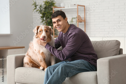 Young man with Australian Shepherd dog sitting on sofa at home