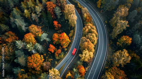 Aerial view of heavy truck on a narrow twisting road. Autumn colorful trees by the sides of the road.