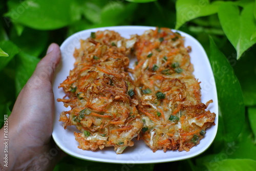 A hand holding a plate of vegetable fritter against green background 