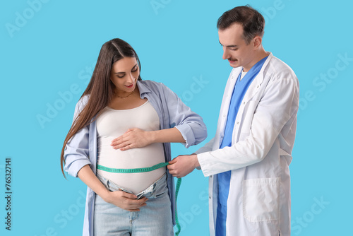 Young pregnant woman with doctor measuring her belly on blue background