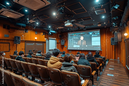 A person in a brown jacket watching a presentation in a lecture hall.