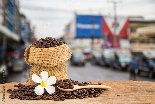 Coffee beans in burlap sack on wooden table with blur background