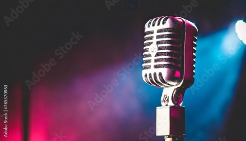 vintage vocal microphone in the dark on a concert stage with pink and blue spot lighting live music or podcast wide banner background with copy space