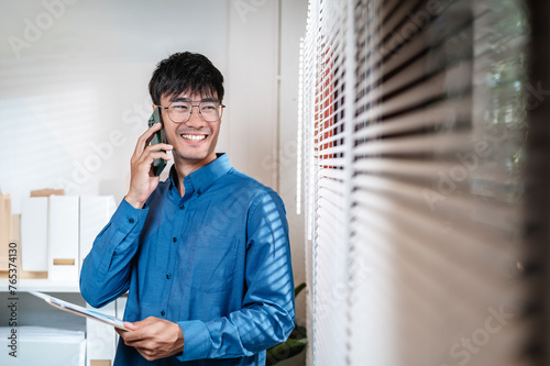 talk, friendly, job, mobile phone, manager, occupation, success, successful, corporate, executive. A man is talking on his cell phone while smiling. He is wearing a blue shirt and glasses.