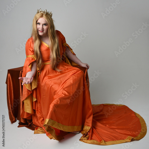 Full length portrait of plus size blonde woman, wearing historical medieval fantasy gown, golden crown royal queen. sitting pose on throne chair, isolated studio background.