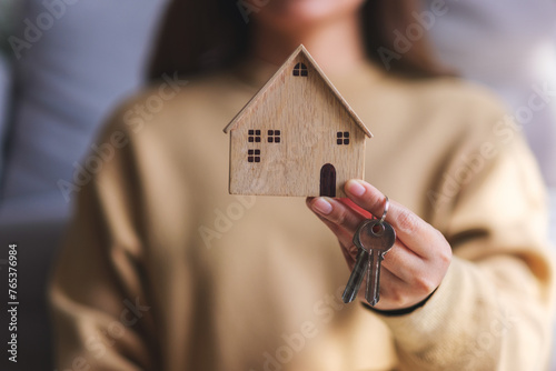 Closeup image of a woman holding a wooden house model and the keys for real estate concept