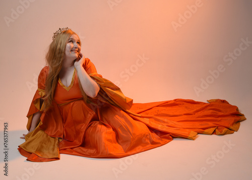 Full length portrait of plus size blonde woman, wearing historical medieval fantasy gown, golden crown royal queen. sitting pose isolated studio background.