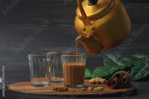 Fresh milk masala tea or Indian Kadak Chai.  Herbal tea in glass cups. Locally called mini cutting chai or cutting chai or masala chai. Indian chai in glass cups with metal kettle and other masalas 
