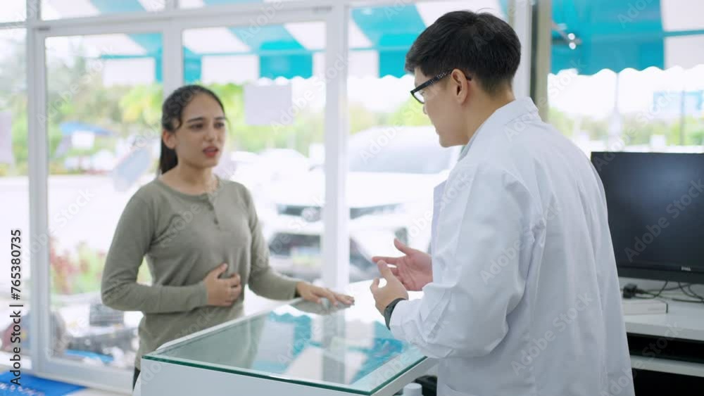 Asian man pharmacist medication recommendation about medicine, drugs and supplements to woman patient with stomach ache customer in drugstore. Medical pharmacy and healthcare providers concept. Asian man pharmacist medication recommendation about medicine, drugs and supplements to woman patient with stomach ache customer in drugstore. Medical pharmacy and healthcare providers concept.
