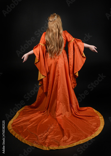 Full length portrait of plus sized woman blonde hair, wearing historical medieval fantasy gown, golden crown of royal queen. Standing pose, walking away in silhouette, isolated dark studio background.