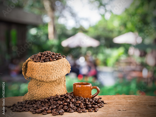 Coffee beans in burlap sack on wooden of blurred coffee shop background