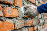 Bricklayer installing brick masonry on an exterior wall with a trowel and putty knife