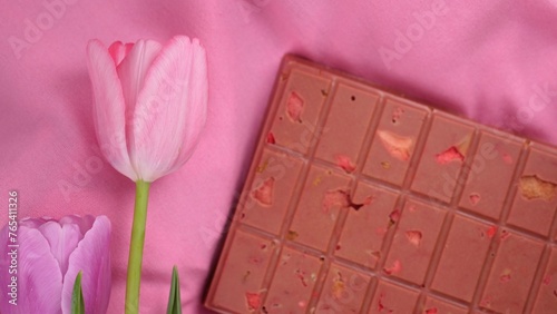 Fototapeta Naklejka Na Ścianę i Meble -  A bar of pink ruby chocolate with sublimated freeze-dried strawberries and almonds and spring tulip flowers . A dessert based on berries and nuts for International Women's Day, March 8, mother's day