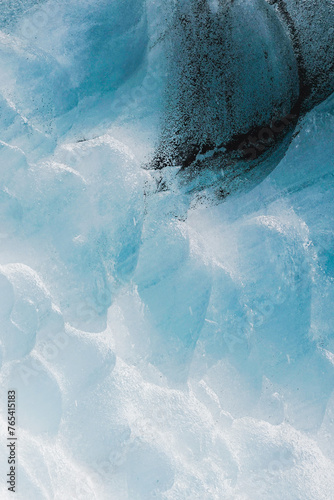 Textured wall of ice inside a glacier covered in black ash