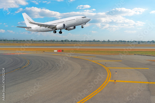 View of the turn from the taxiway onto the runway and a passenger jet plane taking off against the background