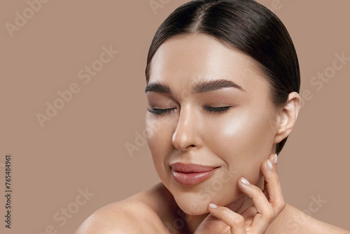 Beauty face. Woman with natural makeup and healthy skin portrait. Beautiful girl model touching fresh glowing hydrated facial skin on beige background