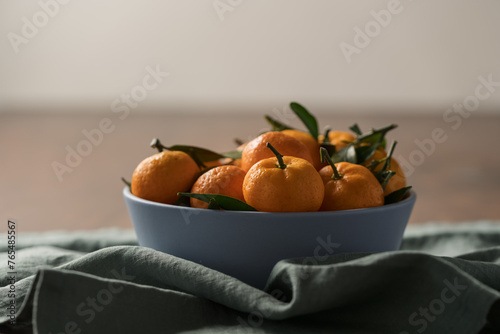 Fototapeta Naklejka Na Ścianę i Meble -  Small organic tangerines with leaves in ceramic bowl on wood table