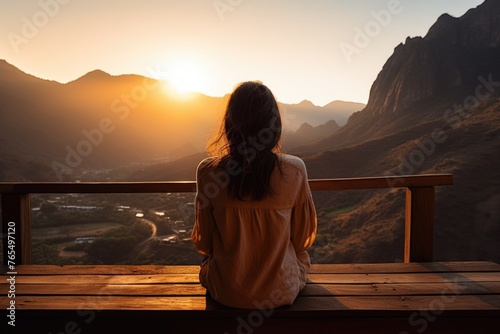 Woman sits on wooden bench overlooking mountain range