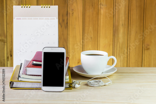 Smart phone,coffee cup,and stack of book with calendar on wooden table