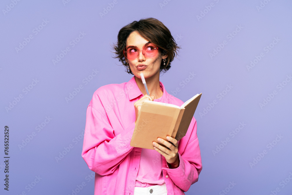 Young stylish woman, wearing sunglasses, with a serious facial expression, holding a pen and diary Young stylish woman, wearing sunglasses, with a serious facial expression, holding a pen and diary