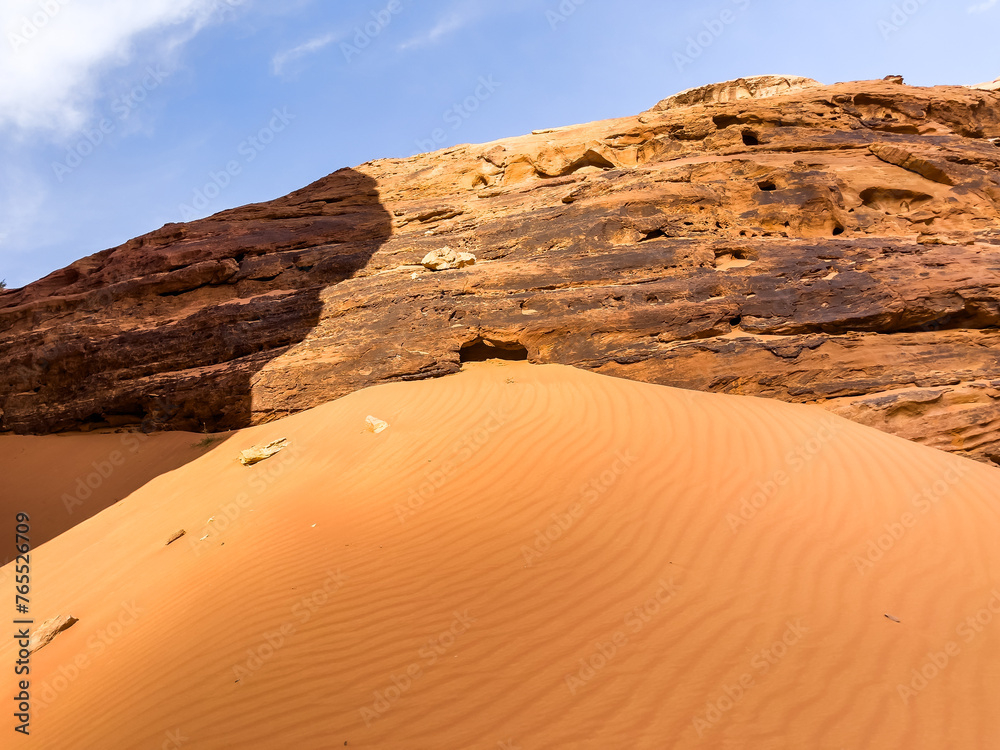 A sandy cliff in the desert with an amazing rock formation behind it under the blue cloudy sky A sandy cliff in the desert with an amazing rock formation behind it under the blue cloudy sky