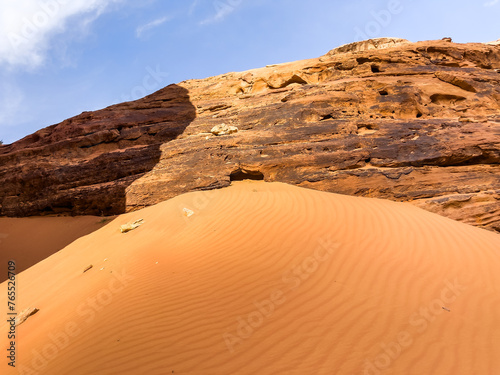 A sandy cliff in the desert with an amazing rock formation behind it under the blue cloudy sky