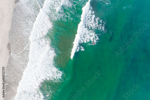 drone aerial overhead view of a surfer with a red surfboard in a sea of turquoise water