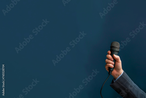 main tenant un microphone, ou micro d'un homme portant un costume et une chemise. Fond bleu canard foncé (teal)  avec espace négatif copy space. Droit de parole, liberté de la Presse photo